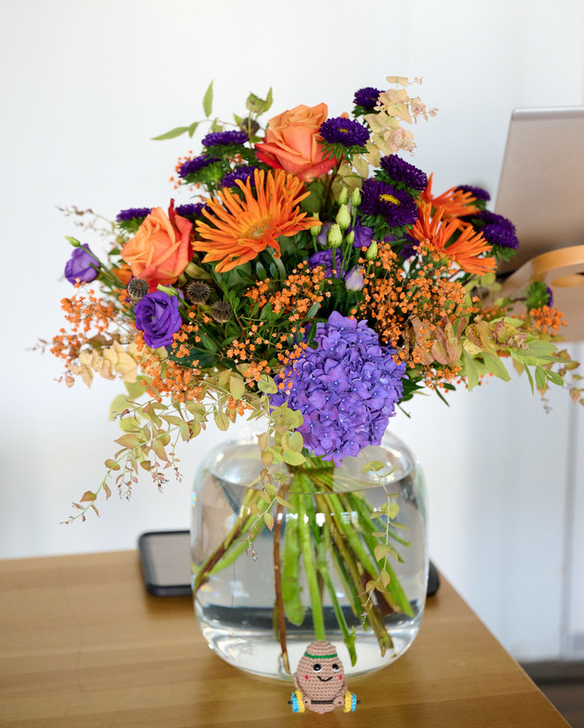 Bunter Blumenstrauss mit orangefarbenen und violetten Blüten in einer Glasvase.
