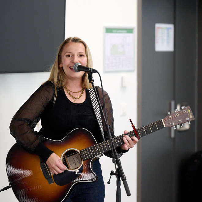 Frau singt und spielt Akustikgitarre vor einem Mikrofon.