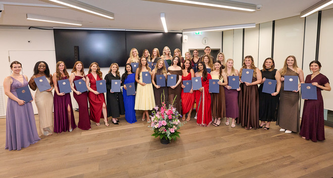 Absolventinnen posieren in festlicher Kleidung mit ihren Diplomen für ein Gruppenfoto.