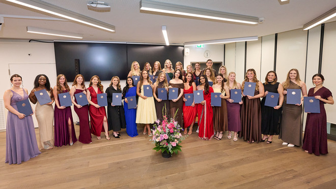 Absolventinnen posieren in festlicher Kleidung mit ihren Diplomen für ein Gruppenfoto.